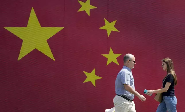 People walk in front of a Chinese national flag in Belgrade, Serbia, Tuesday, May 7, 2024. Chinese leader Xi Jinping's visit to European ally Serbia on Tuesday falls on a symbolic date: the 25th anniversary of the bombing of the Chinese Embassy in Belgrade during NATO's air war over Kosovo. (AP Photo/Darko Vojinovic)