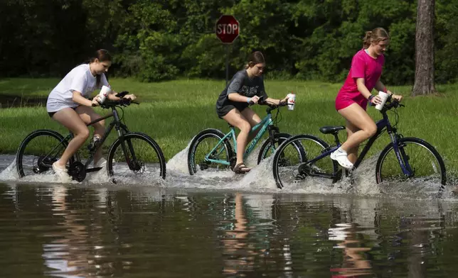 Girls ride their bikes through flood water near the bridge over Lake Houston along West Lake Houston Parkway after it was closed due to high water on either side of the thoroughfare, Saturday, May 4, 2024, in Kingwood, Texas. (Jason Fochtman/Houston Chronicle via AP)