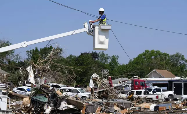 A worker fixes a line above debris from tornado damaged homes, Wednesday, May 22, 2024, in Greenfield, Iowa. (AP Photo/Charlie Neibergall)
