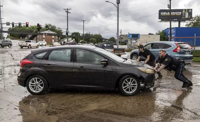 A police officer and an employee of nearby Dingman's Collision Center push a car that had been caught in flood waters in Omaha, Neb. on Tuesday, May 21, 2024 (Chris Machian /Omaha World-Herald via AP)