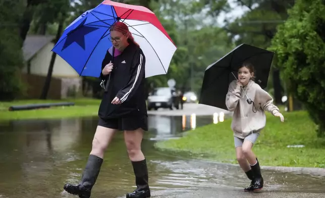 Amanda Kovar and her daughter, Zoe, walk through their neighborhood in North Woodland Hills to survey the area after severe flooding, Thursday, May 2, 2024, in the Houston neighborhood of Kingwood, Texas. (Jason Fochtman/Houston Chronicle via AP)
