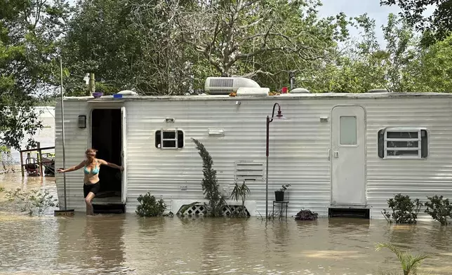 A woman steps out of a mobile home in an unincorporated area in east Harris County near Houston on Saturday afternoon, May 4, 2024. The mobile home was surrounded by flood waters caused by the nearby San Jacinto River, which was overflowing due to heavy rainfall earlier this week. (AP Photo/Juan Lozano)