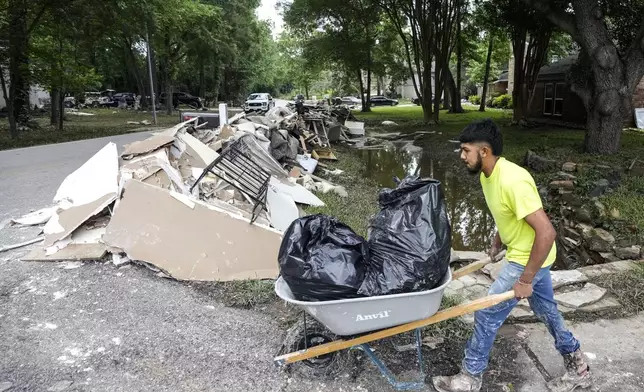 A construction worker moves trash bags full of flood-damaged items to a debris pile while cleaning up from flood damage in the River Plantation neighborhood on Monday, May 6, 2024 in Conroe, Texas. (Brett Coomer/Houston Chronicle via AP)