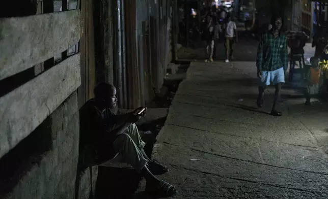 A boy looks at his phone on the street of Bombay at night, Freetown, Sierra Leone, Saturday, April 28, 2024 Sierra Leone declared a war on the cheap synthetic drug, calling it an epidemic and a national threat. The drug is ravaging youth, and healthcare services are severely limited. (AP Photo/ Misper Apawu)