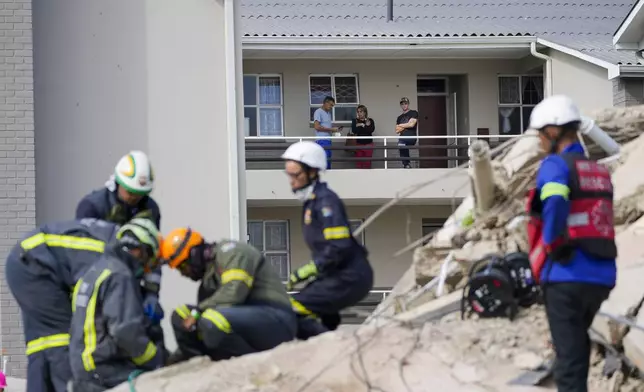 Residents watch rescue workers search the site of a building collapse in George, South Africa, Wednesday, May 8, 2024. Rescue teams are searching for dozens of construction workers missing after a multi-story apartment complex collapsed in the coastal city have brought out more survivors as the operation entered a second night of desperate work to find anyone alive in the mangled wreckage. (AP Photo/Jerome Delay)