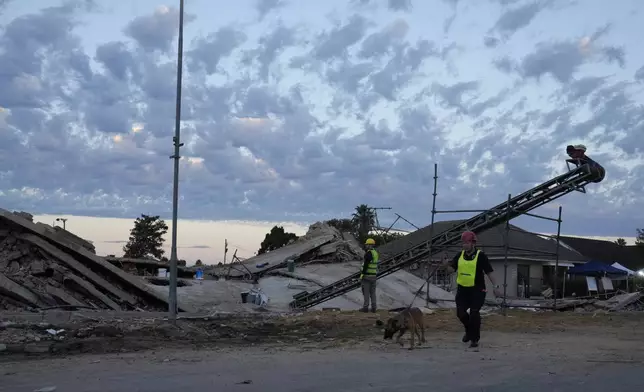 A rescue worker walks with a sniffer dog at the site of a building collapse in George, South Africa, Wednesday, May 8, 2024. Rescue operations continue for dozens of construction workers missing. (AP Photo/Nardus Engelbrecht)