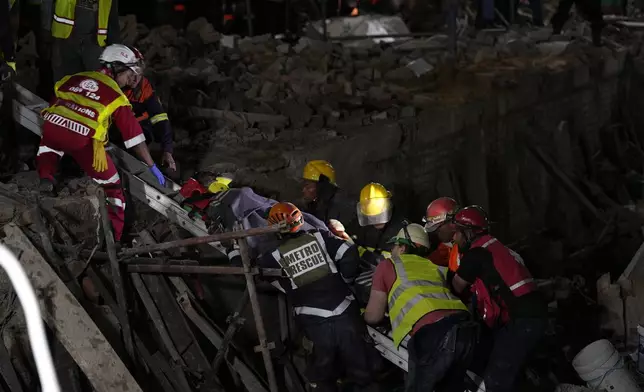 A survivor is bought to the surface at the scene of a building collapse in the city of George, about 400 kilometers (250 miles) east of Cape Town, South Africa, Tuesday, May 7, 2024. Rescue teams trying to find dozens of construction workers missing since a multi-story apartment complex collapsed in a coastal city in South Africa have made contact with 11 people buried alive beneath the mangled wreckage, authorities said Tuesday. (AP Photo/Nardus Engelbrecht)