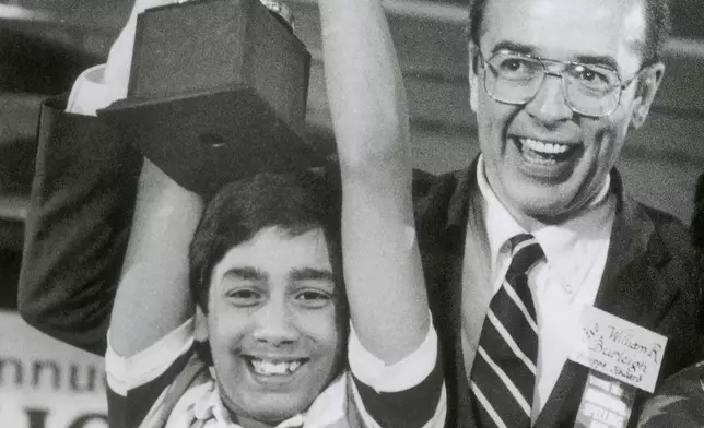 FILE - Balu Natarajan, an 8th grade student at Jefferson Junior High School in Woodbridge, Ill., holds his trophy with the aid of William R. Burleigh, vice president of Scripps Howard Newspapers, sponsor of the National Spelling Bee, after he won the competition in Washington, on June 6, 1985. Since 1999, 28 of the last 34 Scripps National Spelling bee champions have been Indian American. And most of those winners are the offspring of parents who arrived in the United States on student or work visas. The experiences of first-generation Indian Americans and their spelling bee champion children illustrate the economic success and cultural impact of the nation’s second-largest immigrant group. (AP Photo/Bob Daugherty, File)