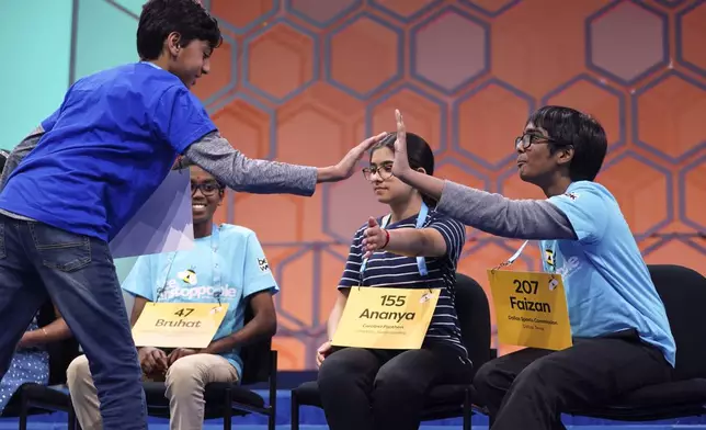 Shrey Parikh, 12, of Rancho Cucamonga, Calif., left, high-fives Ananya Rao Prassanna, 13, of Apex, N.C., second from right, and Faizan Zaki, 12, of Allen, Texas, right, while competing during the finals of the Scripps National Spelling Bee, in Oxon Hill, Md., Thursday, May 30, 2024. (AP Photo/Nathan Howard)