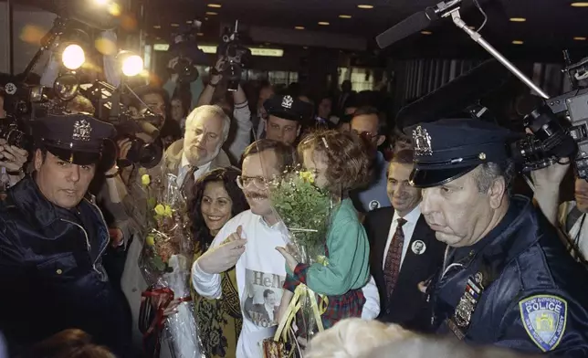 FILE - Former hostage Terry Anderson, center, carries his daughter Sulome, 6, through a crunch of media upon arrival to John F. Kennedy International Airport in New York, Dec. 10, 1991. At left is Sulome's mother, Madeleine Bassil, and at immediate right is Associated Press President Lou Boccardi. Fellow former hostages, family, and coworkers celebrated the life of journalist and philanthropist Terry Anderson, Wednesday, May 8, 2024, as a man who helped others while struggling to heal himself. (AP Photo/Ed Bailey, File)
