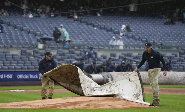 Members of the grounds crew cover the field during a rain delay in the eighth inning of the baseball game between the New York Yankees and the Detroit Tigers at Yankee Stadium, Sunday, May 5, 2024, in New York. (AP Photo/Seth Wenig)