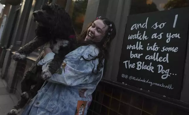 Taylor Swift fan Brodie MacArthur from east London poses with a friend's dog next to a sign featuring Taylor Swift lyrics outside The Black Dog pub in Vauxhall, London, Saturday, May 4, 2024. As Taylor Swift prepares to launch the Europe leg of her blockbuster Eras tour, thousands of her fans from the U.S. and Canada are following her across the pond. (AP Photo/Alastair Grant)