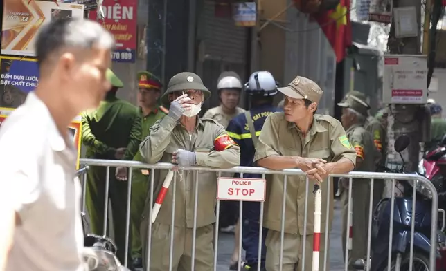 Security officers guard at the cordoned off entrance to the site of a fire in Hanoi, Vietnam Friday, May 24, 2024. State media said the overnight fire in a small apartment building has killed a number of people and injured several others. (AP Photo/Hau Dinh)