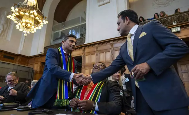 South Africa's agents Vusimuzi Madonsela, seated, and Cornelius Scholtz, left, are greeted as they wait for the start of hearings at the International Court of Justice, in The Hague, Netherlands, Thursday, May 16, 2024. The U.N.'s top court opened two days of hearings in a case brought by South Africa to see whether Israel needs to take additional measures to alleviate the suffering in war-ravaged Gaza. (AP Photo/Peter Dejong)