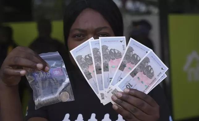 A woman holds the new Zimbabwean banknotes and coins called the ZiG, in the streets of Harare, Zimbabwe, Tuesday, April 30, 2024. Zimbabwe started circulating banknotes and coins for another new currency Tuesday in its latest attempt to solve a long-running and at times baffling monetary crisis that has seen the government try gold coins and a digital currency among other ideas. (AP Photo/Tsvangirayi Mukwazhi)