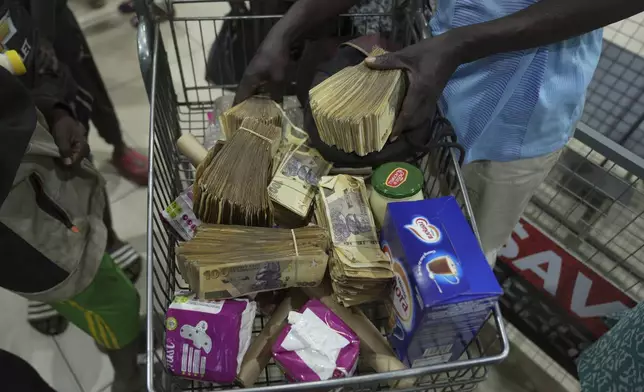 A man uses old Zimbabwean dollar notes to buy groceries in a supermarket in Harare, Thursday, April 25, 2024. Zimbabwe started circulating banknotes and coins for another new currency Tuesday in its latest attempt to solve a long-running monetary crisis that has seen the government try gold coins and a digital currency among other ideas. (AP Photo/Tsvangirayi Mukwazhi)