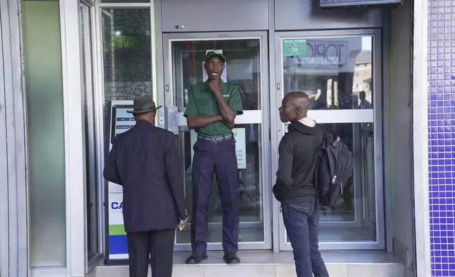A security guard stands outside a bank while waiting for clients to enter and withdraw the new Zimbabwean banknotes called the ZiG, in the streets of Harare, Zimbabwe, Tuesday, April 30, 2024. Zimbabwe started circulating banknotes and coins for another new currency Tuesday in its latest attempt to solve a long-running and at times baffling monetary crisis that has seen the government try gold coins and a digital currency among other ideas. (AP Photo/Tsvangirayi Mukwazhi)