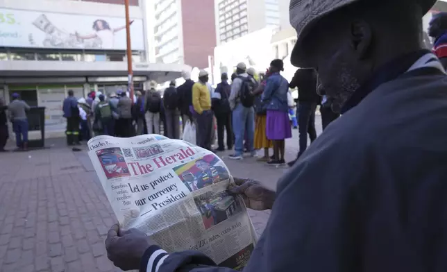 A man reads a Newspaper while waiting in a queue to withdraw the new Zimbabwean banknotes called the ZiG, in the streets of Harare, Zimbabwe, Tuesday, April 30, 2024. Zimbabwe started circulating banknotes and coins for another new currency Tuesday in its latest attempt to solve a long-running and at times baffling monetary crisis that has seen the government try gold coins and a digital currency among other ideas. (AP Photo/Tsvangirayi Mukwazhi)