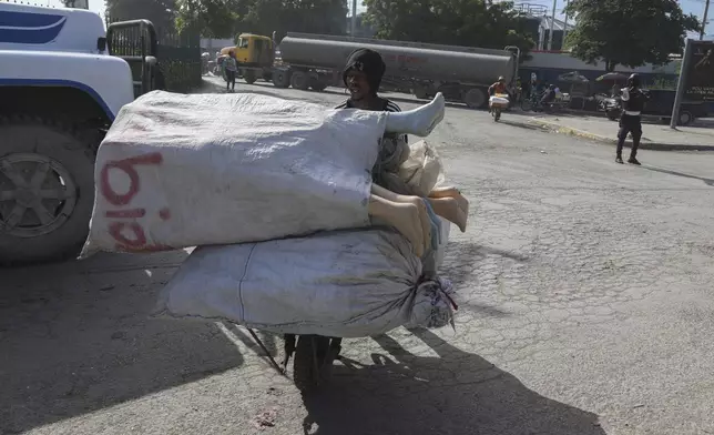 A clothing vendor pushes a wheelbarrow of mannequins through an intersection patrolled by police to place at his streetside stall in Port-au-Prince, Haiti, Monday, June 24, 2024. (AP Photo/Odelyn Joseph)