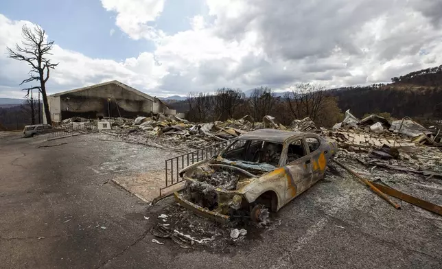 A charred car and the remains of the Swiss Chalet Hotel are pictured after being destroyed by the South Fork Fire in the mountain village of Ruidoso, N.M., Saturday, June 22, 2024. (AP Photo/Andres Leighton)