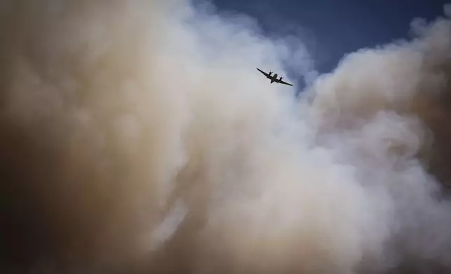 An air tanker soars through a large plume of smoke over and around wildfire-affected areas in the village of Ruidoso, N.M., Tuesday, June 18, 2024. (Chancey Bush/The Albuquerque Journal via AP)