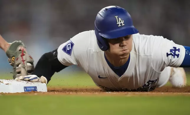 Los Angeles Dodgers designated hitter Shohei Ohtani safely dives back to first base during the eighth inning of a baseball game against the Los Angeles Angels in Los Angeles, Friday, June 21, 2024. (AP Photo/Ashley Landis)