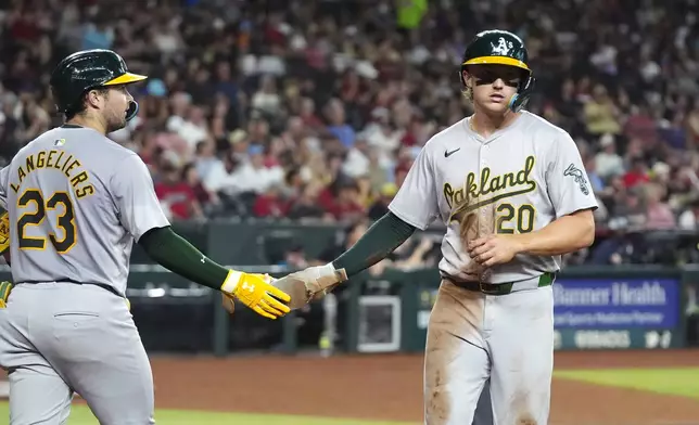 Oakland Athletics' Zack Gelof (20) slaps hands with teammate Shea Langeliers (23) after scoring against the Arizona Diamondbacks during the third inning of a baseball game Friday, June 28, 2024, in Phoenix. (AP Photo/Ross D. Franklin)
