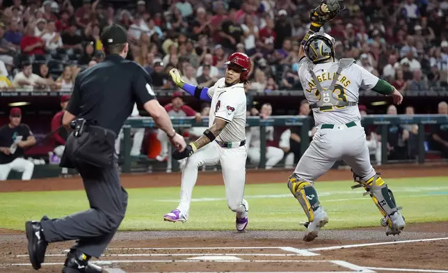 Arizona Diamondbacks' Ketel Marte, center, avoids Oakland Athletics catcher Shea Langeliers, right, to score as umpire Alex Tosi, left, moves during the play during the first inning of a baseball game Friday, June 28, 2024, in Phoenix. (AP Photo/Ross D. Franklin)