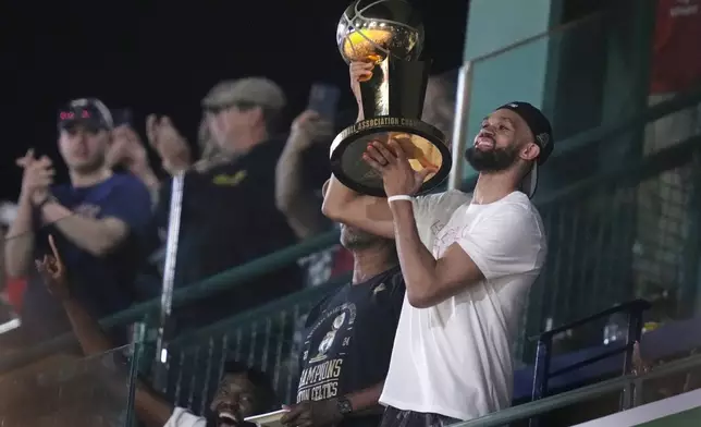 Boston Celtics' Derrick White lifts the Larry O'Brien Championship Trophy during the eighth inning of a baseball game between the Boston Red Sox and the Toronto Blue Jays at Fenway Park, Monday, June 24, 2024, in Boston. (AP Photo/Charles Krupa)