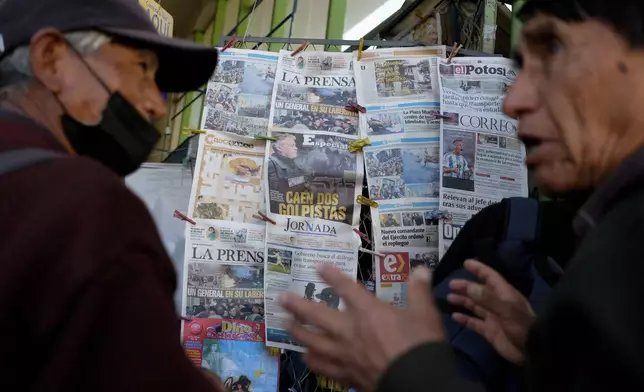 Men talk in front of a newspaper kiosk in La Paz, Bolivia, Thursday, June 27, 2024, a day after Army troops stormed the government palace in what President Luis Arce called a coup attempt. (AP Photo/Carlos Sanchez)