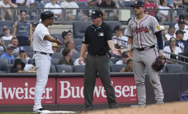 New York Yankees third base coach Luis Rojas, left, argues with the umpire, center, about a tagging call against Anthony Volpe during the sixth inning of a baseball game against the Atlanta Braves, Sunday, June 23, 2024, in New York. (AP Photo/Pamela Smith)