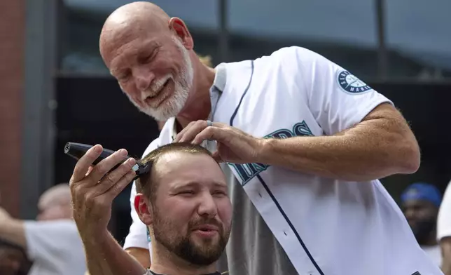 Seattle Mariners catcher Cal Raleigh has his head shaved by former Mariner Jay Buhner on Buhner Buzz Night, Thursday, June 13, 2024, in Seattle. The promotion is based on former Buhner's shaved-head style. (AP Photo/John Froschauer)