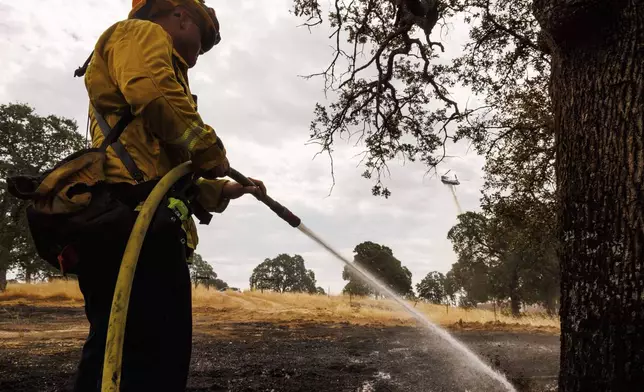 A firefighter uses a hose while a helicopter drops water as the Apache Fire burns in Palermo, Calif., on Tuesday, Jun. 25, 2024. According to Cal Fire, more than a dozen new fires sparked by lightning. (AP Photo/Ethan Swope)