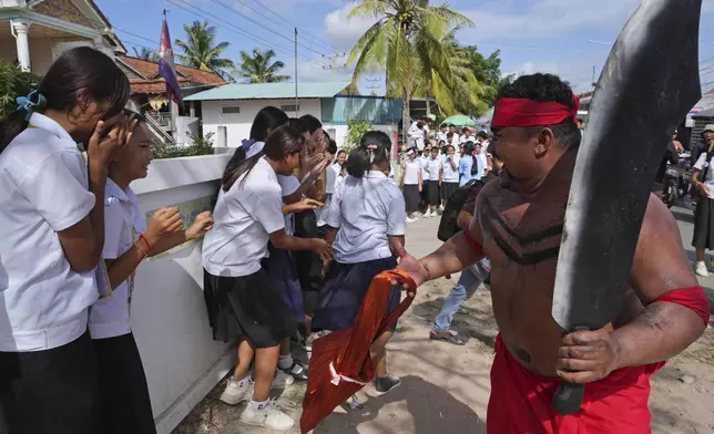 Schoolchildren react to a man, dressed to represent spirits, during the He Neak Ta rituals in Phum Boeung village, northwest of Phnom Penh, Cambodia, Tuesday, June 11, 2024. Cambodian villagers on Tuesday took part in a rare traditional guardian spirit ceremony praying for good fortune, rain and prosperity, as they aimed to preserve this ancient tradition. (AP Photo/Heng Sinith)