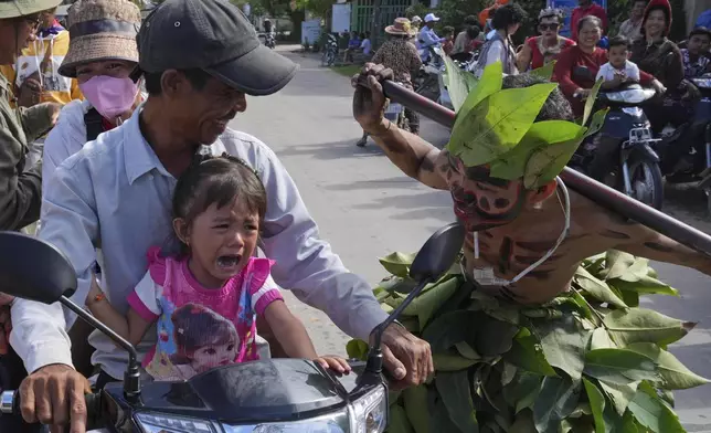 A child cries as she reacts to a man, his face painted in the likeness of a spirit, participating in the He Neak Ta rituals in Phum Boeung village, northwest of Phnom Penh, Cambodia, Tuesday, June 11, 2024. (AP Photo/Heng Sinith)