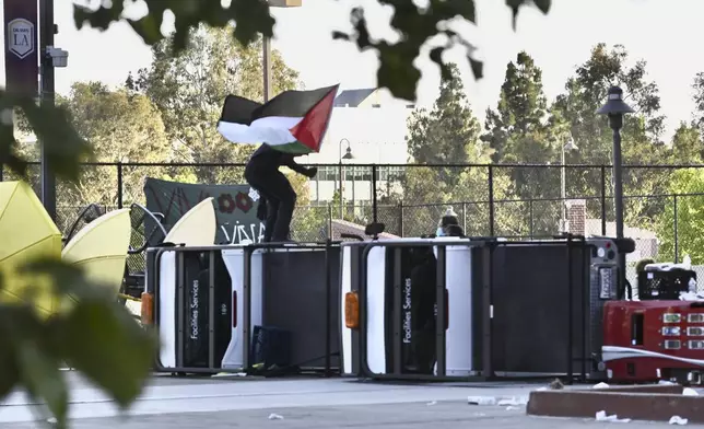 A pro-Palestinian student protester waves a Palestinian flag atop turned over utility carts while awaiting for their divestment demands of California State University, Los Angeles administration on the campus in Los Angeles on Wednesday, June 12, 2024. (Keith Birmingham/The Orange County Register via AP)