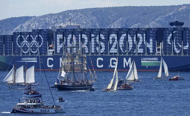 FILE - The Belem, the three-masted sailing ship bringing the Olympic flame from Greece, center, sails past a containership decorated with the Paris 2024 logo when approaching Marseille, southern France, May 8, 2024. (AP Photo/Laurent Cipriani, File)