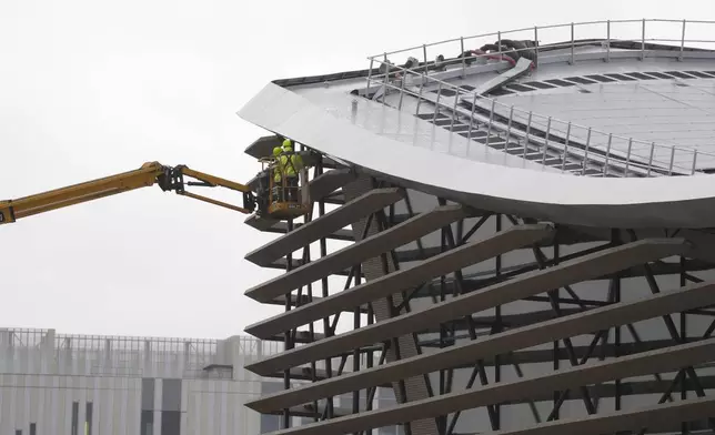 FILE - Workers stand on a crane at the Olympic Aquatic Center near solar panels, Thursday, Dec. 28, 2023, in Saint-Denis, outside Paris. The center will host the artistic swimming, water polo and diving events during the Olympic Games. (AP Photo/Lewis Joly, File)