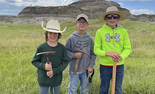 In this image provided by Giant Screen Films, Liam Fisher, Kaiden Madsen and Jessin Fisher pose for a celebratory photo on the day their fossil find was determined to be a juvenile T. rex, in North Dakota. A documentary film crew captured the moment of discovery for the film "T.REX." (David Clark/Giant Screen Films via AP)