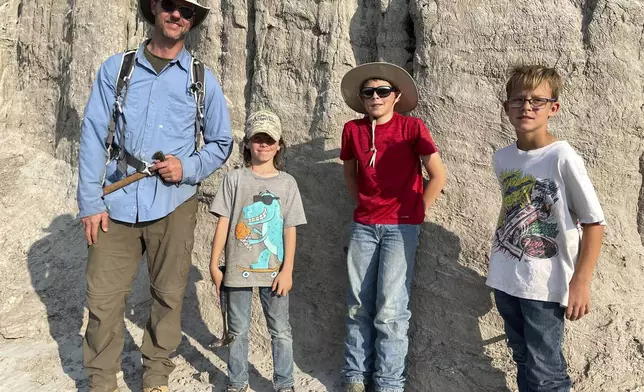 In this photo provided by Giant Screen Films, vertebrate paleontologist Tyler Lyson, left, poses with young fossil finders Liam Fisher, Jessin Fisher and Kaiden Madsen on the day their expedition uncovered diagnostic features of a juvenile T. rex the boys discovered in the Badlands of North Dakota. A documentary film caught the moment of discovery on camera. (David Clark/Giant Screen Films via AP)