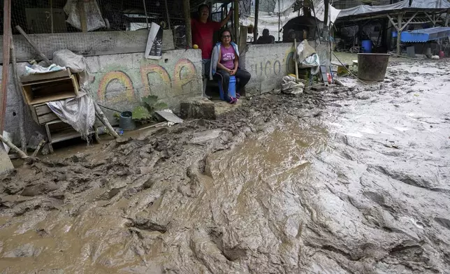 Residents sit in their houses along a road flooded by a landslide caused by heavy rains in Banos, Ecuador, Monday, June 17, 2024. (AP Photo/Dolores Ochoa)