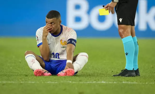 Kylian Mbappe of France sits on the pitch, hand over his bloody nose, as the referee holds the yellow card, during a Group D match between Austria and France at the Euro 2024 soccer tournament in Duesseldorf, Germany, Monday, June 17, 2024. (AP Photo/Andreea Alexandru)