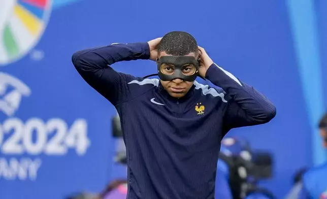 France's Kylian Mbappe adjusts his face mask during the warm up before a Group D match between the Netherlands and France at the Euro 2024 soccer tournament in Leipzig, Germany, Friday, June 21, 2024. (AP Photo/Ariel Schalit)