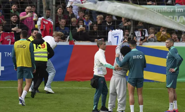 Stewards grab a pitch invader, left, as other pitch invader takes a selfie with Portugal's Cristiano Ronaldo during a training session in Gutersloh, Germany, Friday, June 14, 2024. Portugal will play against Czech Republic during their Group F soccer match at the Euro 2024 soccer tournament on June 18. (AP Photo/Hassan Ammar)