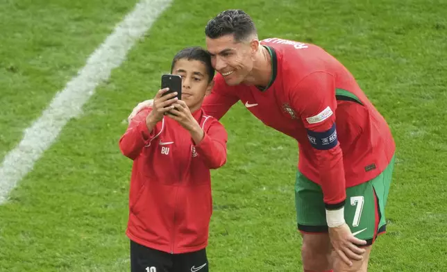 A young pitch invader takes a selfie with Portugal's Cristiano Ronaldo during a Group F match between Turkey and Portugal at the Euro 2024 soccer tournament in Dortmund, Germany, Saturday, June 22, 2024. (AP Photo/Michael Probst)