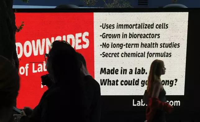 People stand outside the entrance to a pop-up tasting event for "lab-grown" meat produced by Upside Foods, as a protest truck parked out front displays a message advocating against cultivated meat, Thursday, June 27, 2024, in Miami. As Florida's ban on lab-grown meat is set to go into effect next week, one manufacturer hosted a tasting party, serving up cultivated chicken tostadas to dozens of attendees on a rooftop in Miami's Wynwood neighborhood. (AP Photo/Rebecca Blackwell)