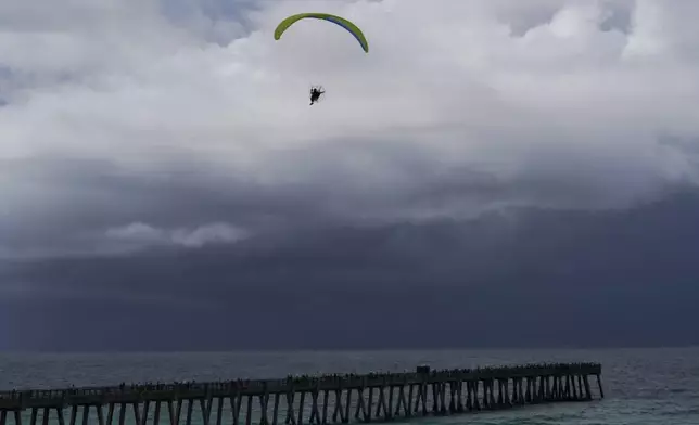 A paraglider flies over Navarre Beach Fishing Pier as storm clouds approach the shore in Navarre Beach, Fla., Sunday, June 16, 2024. (AP Photo/Kiichiro Sato)