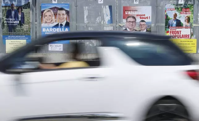 A car drives past electoral posters, Thursday, June 27, 2024 in Strasbourg, eastern France. French President Emmanuel Macron called snap elections following the defeat of his centrist alliance at European Union elections earlier this month. Voters will choose lawmakers for the National Assembly in two rounds on June 30 and July 7. (AP Photo/Jean-Francois Badias)
