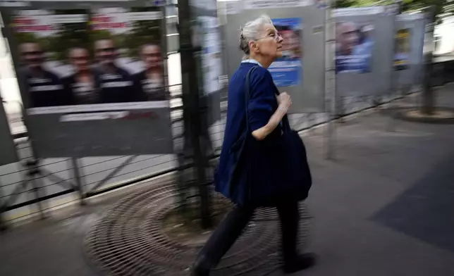 A woman walks past campaign boards for the upcoming parliamentary elections in Paris, Thursday June 27, 2024. Voters will choose lawmakers for the National Assembly in two rounds on June 30 and July 7. (AP Photo/Christophe Ena)