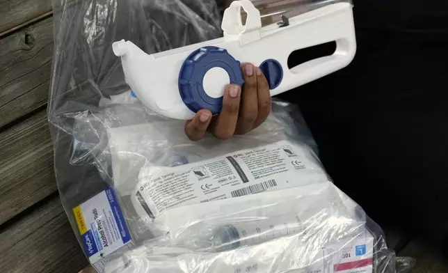 Camden Alderman, 21, who has a rare disease called Wiskott-Aldrich syndrome, holds some of the drugs and medical equipment he uses near his home in Greensboro, N.C., Wednesday, June 12, 2024. (AP Photo/Chuck Burton)